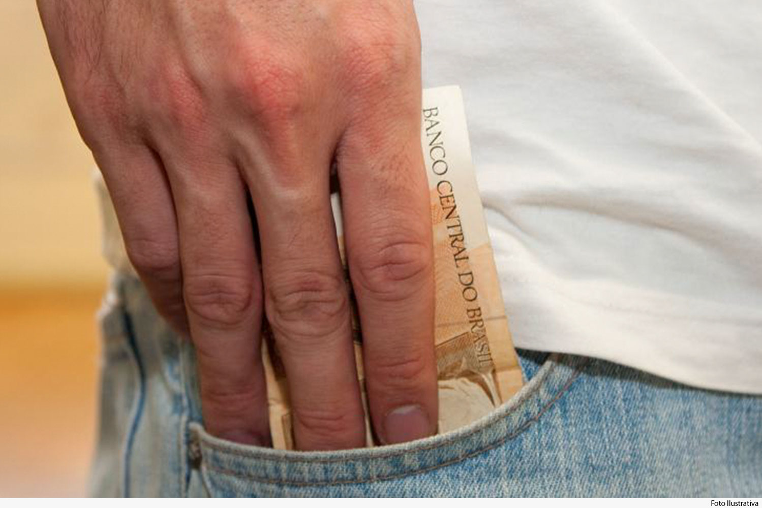 Pessoa do sexo masculino, vestido de jeans e camiseta, retira dinheiro do bolso