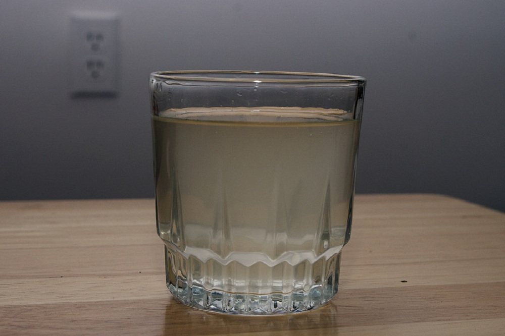 Copo de vidro transparente contendo água turva em cima de mesa