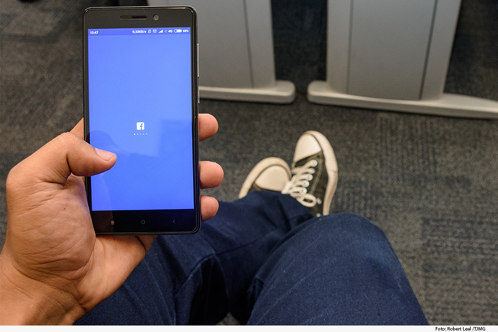 Mão com celular na mão exibindo na tela Facebook