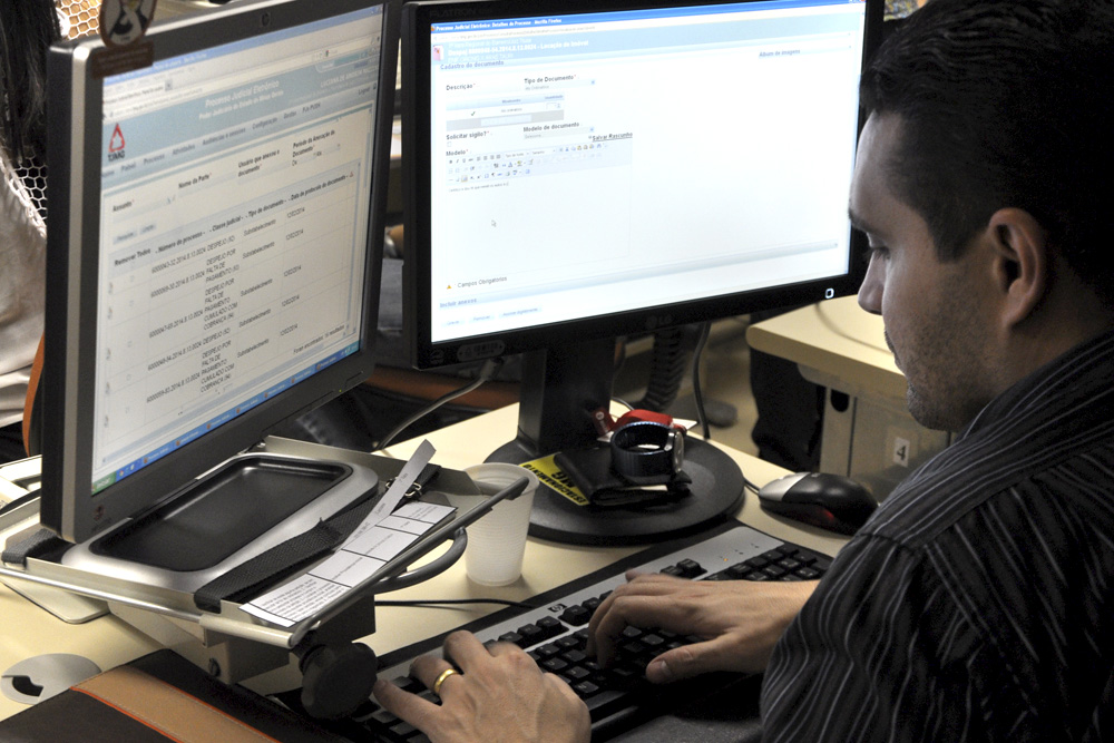 Homem diante do computador, cuja tela mostra sistema PJe