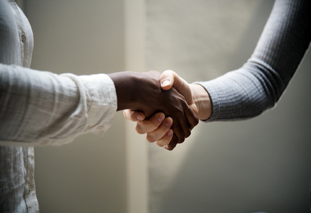 Mão feminina negra e mão masculina branca se apertam