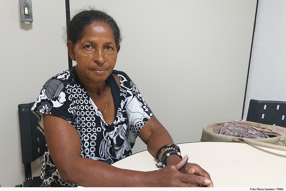 Foto mostra senhora sentada em uma mesa