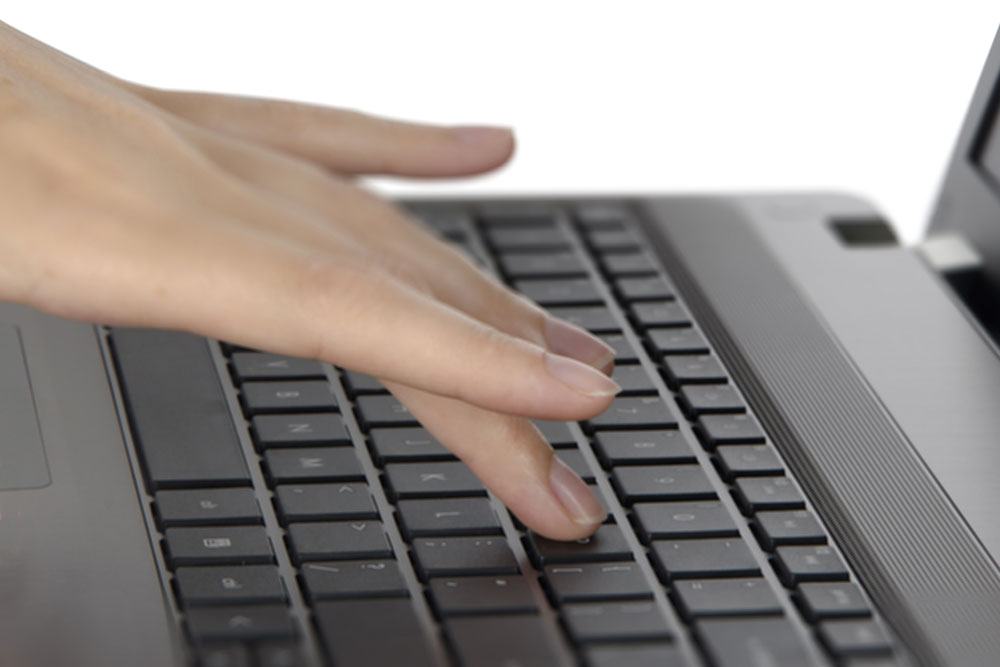 Mão feminina digita em teclado de notebook