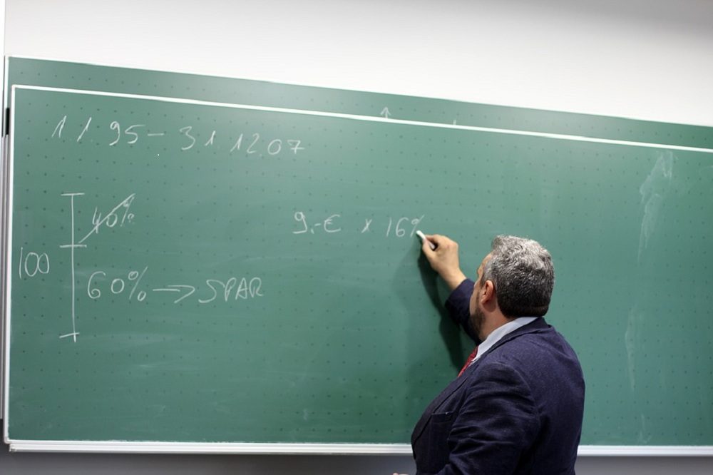 Homem de terno escreve em lousa com cálculos matemáticos