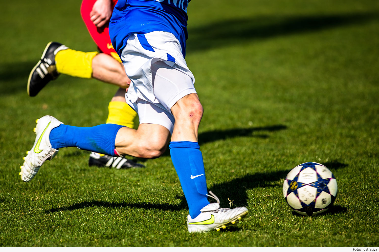 Plano mostrando pernas de jogadores chutando bola em campo de futebol