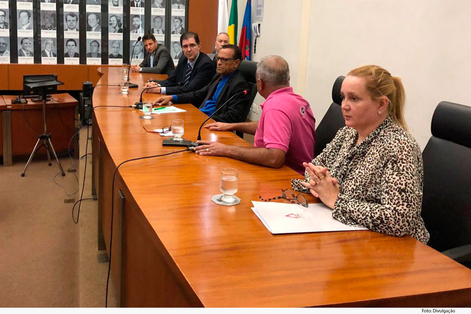 Mesa com microfones e pessoas em evento com palestra