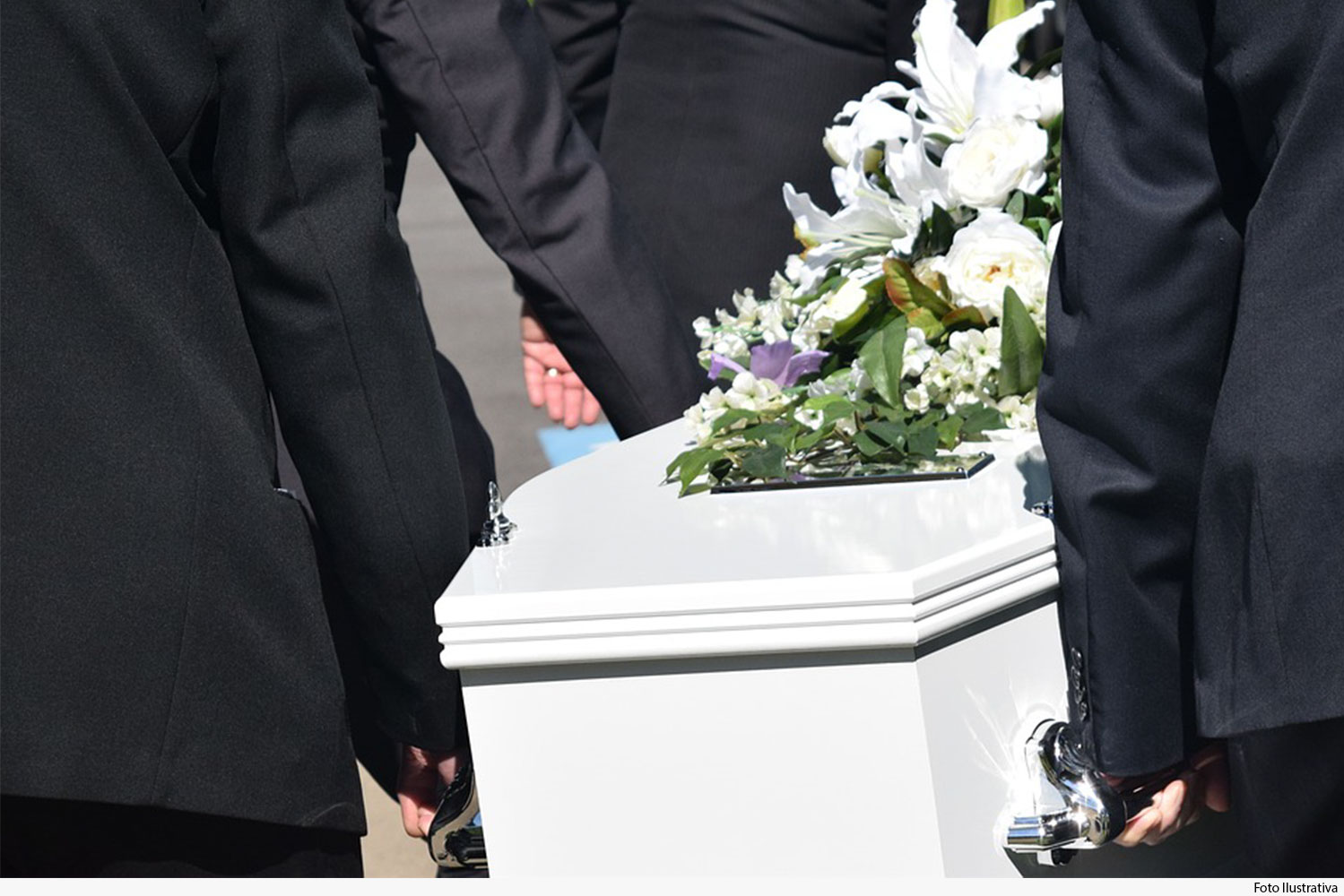 Homens utilizando terno preto,segurando um caixão branco com flores encima