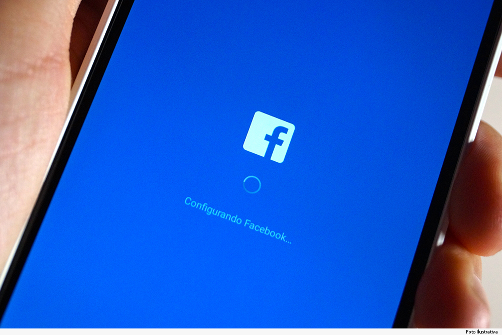 Mão segura smartphone mostrando na tela página do Facebook