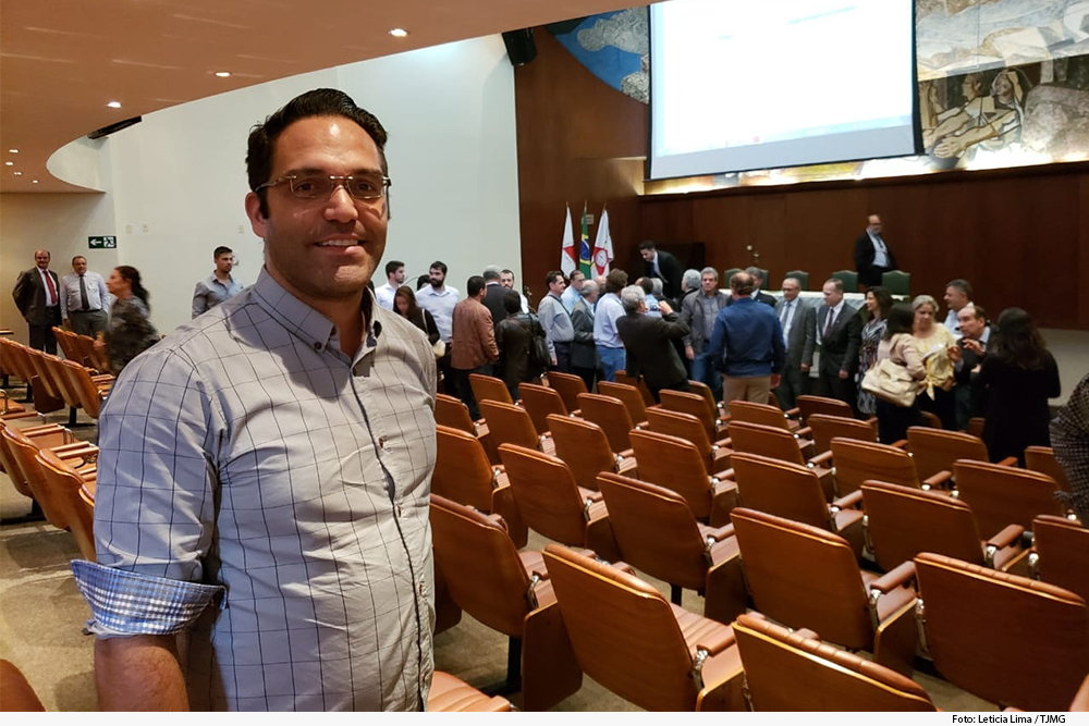 Homem em frente a um auditório, grupo de pessoas e painel