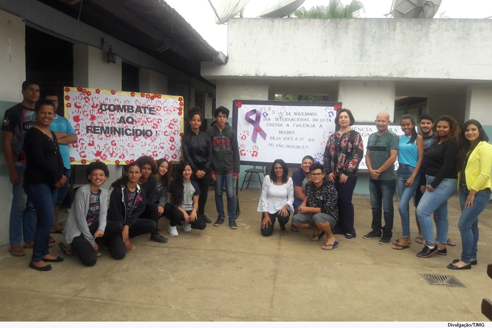 Juíza e alunos de escola, com cartazes sobre feminicídio e proteção da mulher