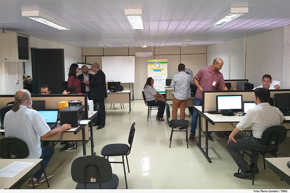 Foto mostra sala com pessoas sentadas e em pé conversando