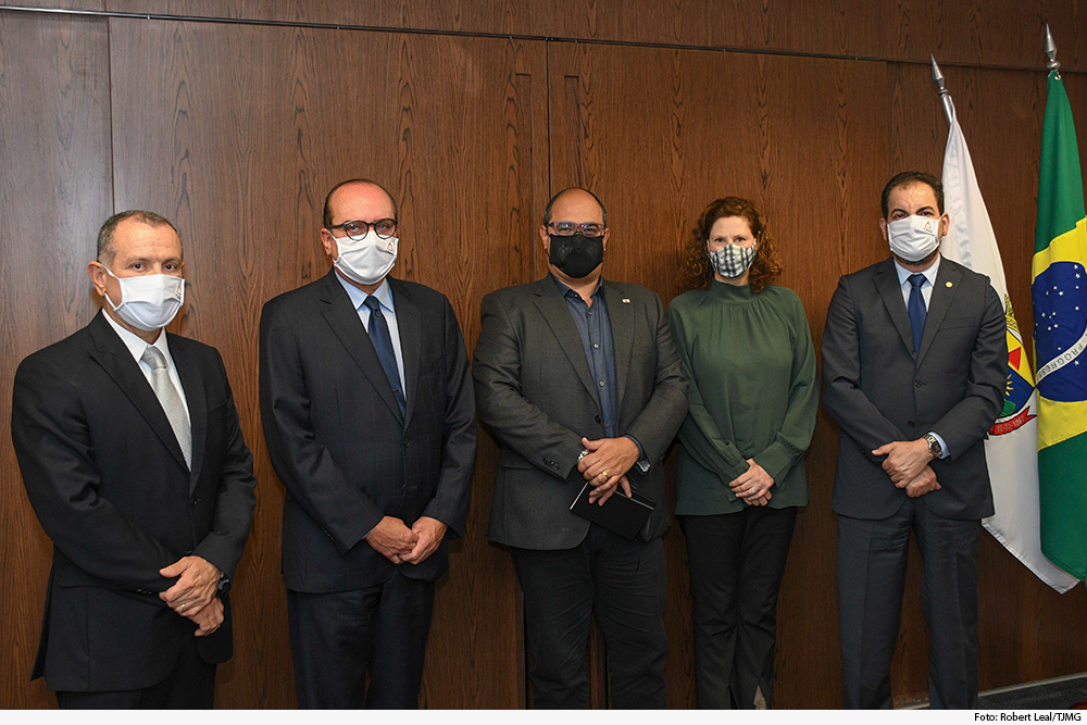 Autoridades de pé, ao lado da bandeira nacional, do Judiciário e de Minas, em gabinete