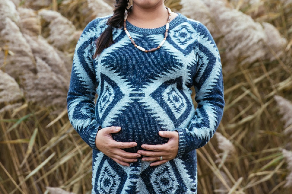 Plano americano de mulher grávida, com plantas ao vento no fundo