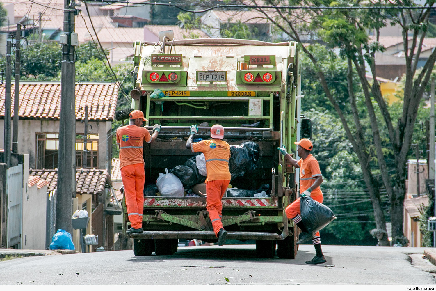 Vista traseira de caminhão de lixo com garis sobre o estribo 