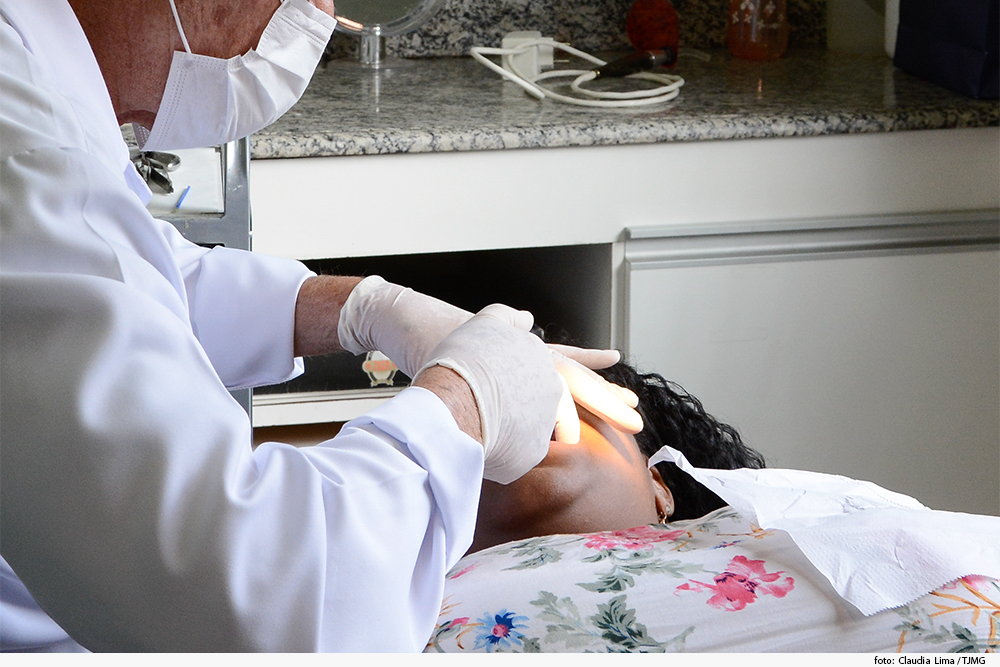 Dentista trata mulher deitada em cadeira odontológica