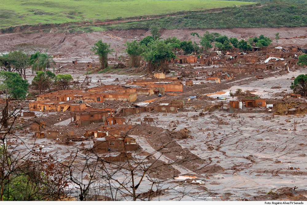 Foto mostra área coberta de lama, com casas e vegetação