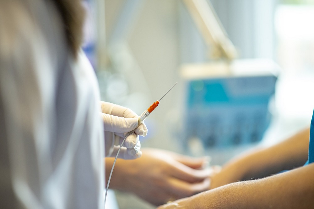 Torso de pessoa com jaleco e estetoscópio segurando seringa e braço de paciente