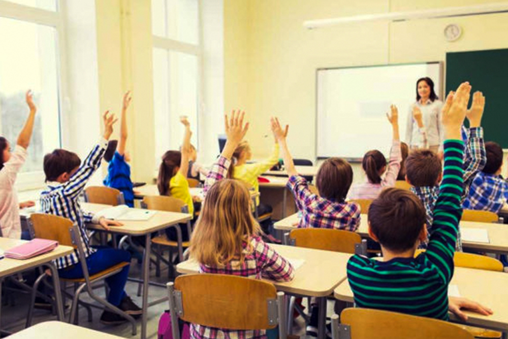 Sala de aula infantil, com crianças levantando as mãos