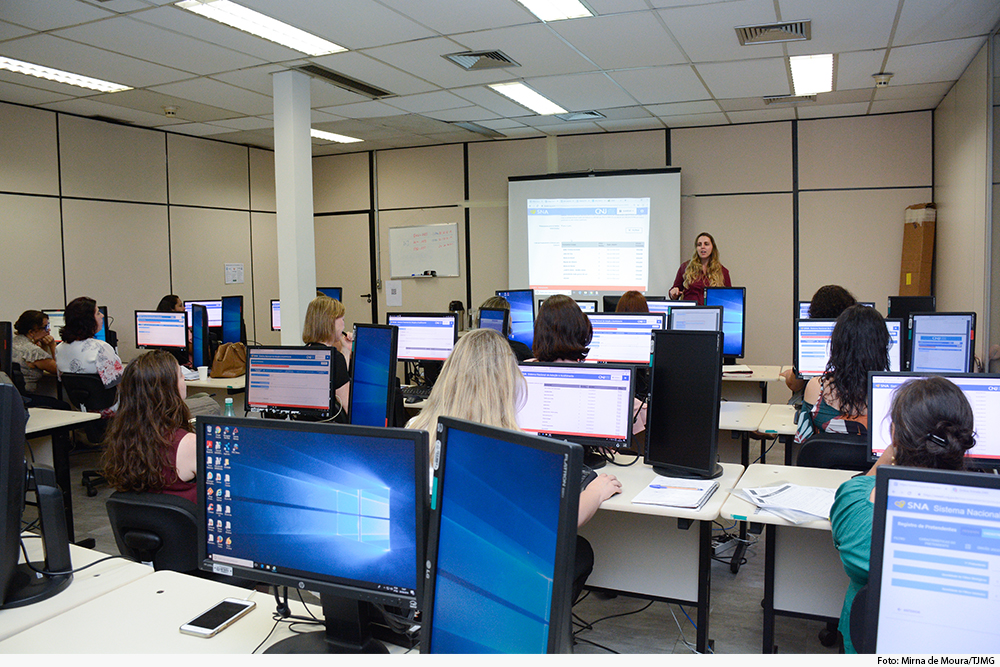 Pessoas fazem curso em laboratório de informática com palestrante de pé, à frente