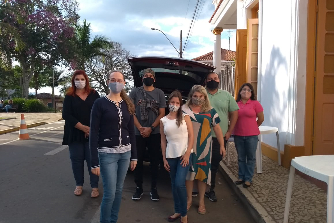Pessoas com doação, em frente a carro, junto a posto de coleta