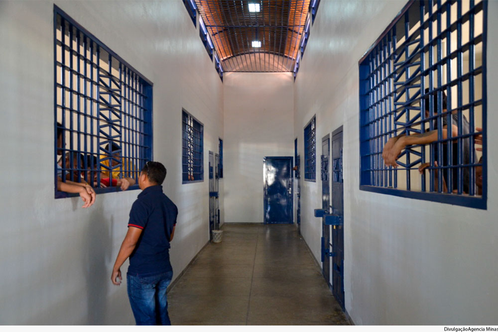 Corredor de unidade de internação de jovens, com funcionário interagindo com adolescente através de grade