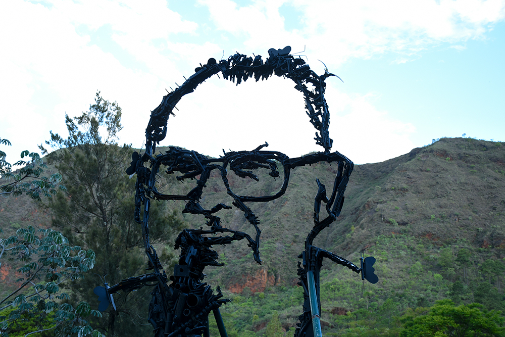 Escultura de rosto de ambientalista tendo ao fundo a Serra do Curral