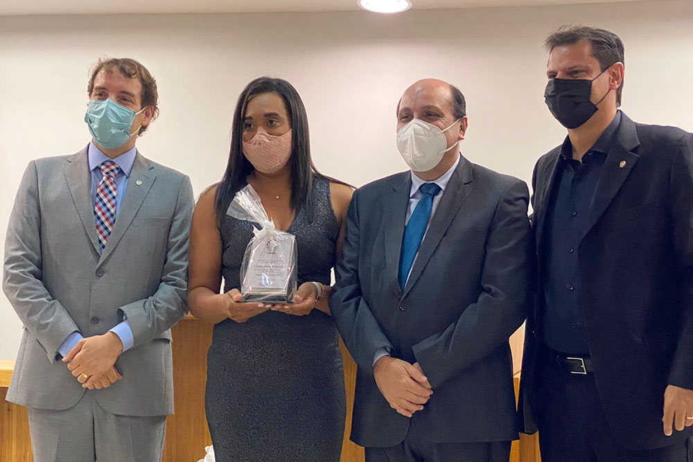 Mulher segura placa ao lado de três magistrados, de terno