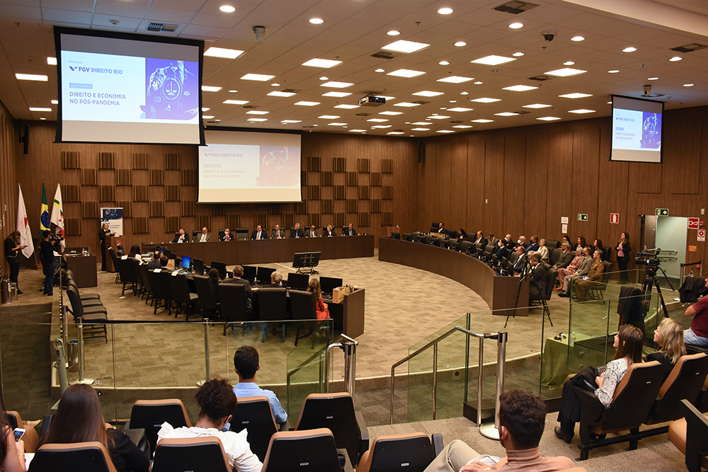 Vista geral do auditório com público, mesa de honra e palestrante