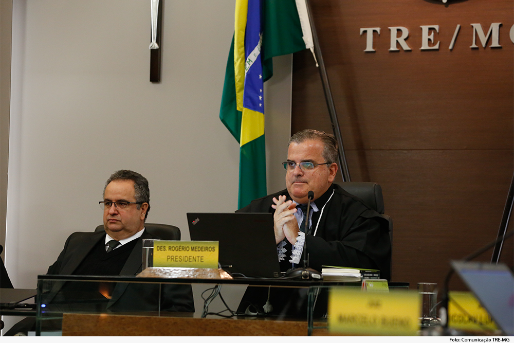 Magistrados em plenário, tendo bandeira nacional e de Minas ao fundo