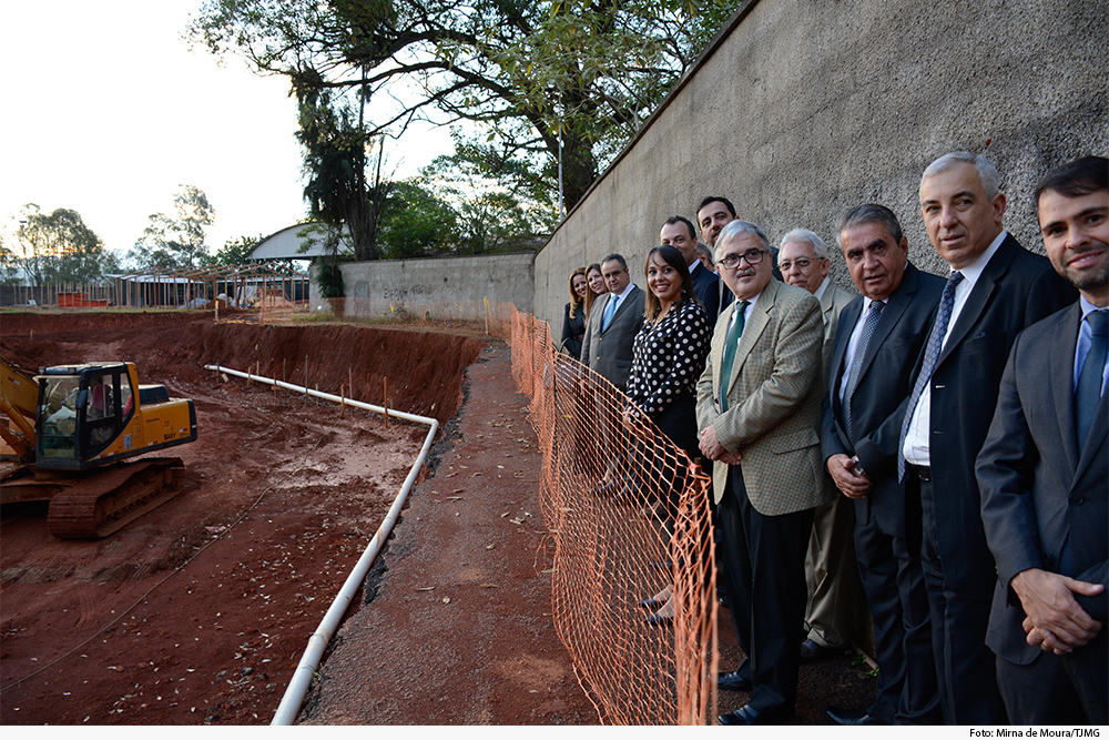 Foto mostra terreno com trator, muro com pessoas encostadas nele