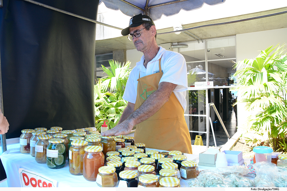 Homem de avental mostrando potes de doces caseiros
