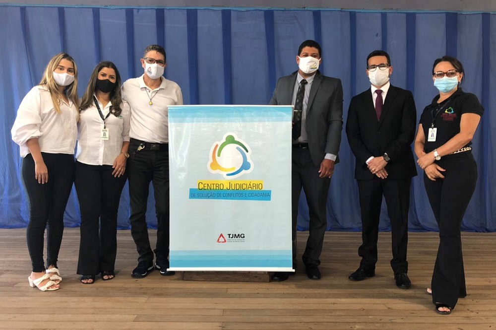 Juiz e servidores em auditório com banner do Cejusc