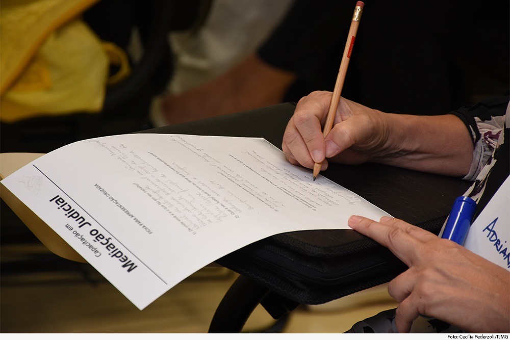 Mão segurando lápis anota em folha de papel com logomarca da Ejef