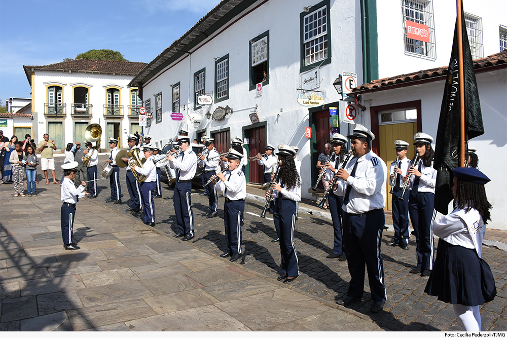 Banda mirim toca em cidade histórica, com casas atrás e ao lado