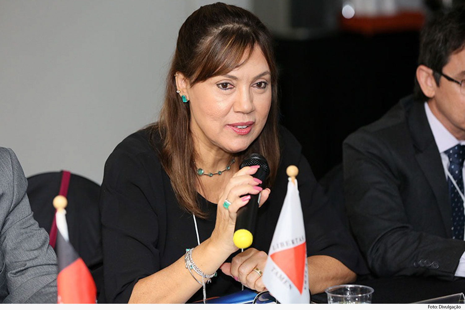Juíza, portando crachá, fala ao microfone em evento