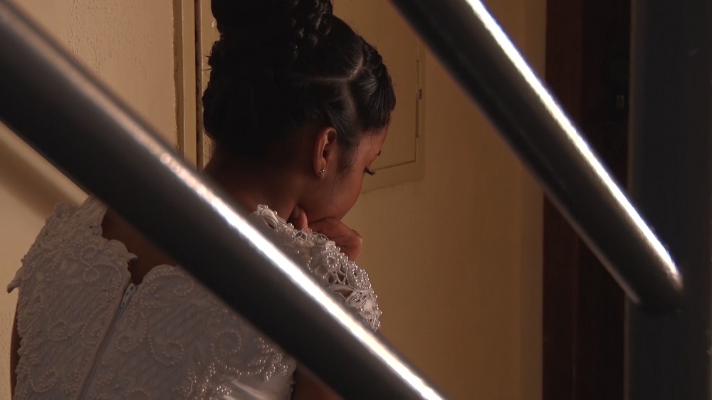 Criança vestida de noiva sentada em escada, de perfil