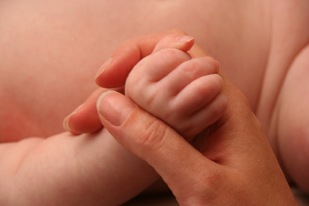 Mão de adulto pegando mão de bebê