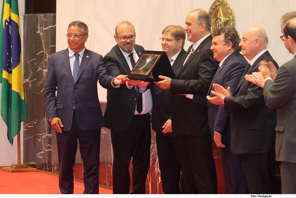 Desembargador Jair VarÃ£o, ao centro, recebe placa de cidadÃ£o honorÃ¡rio. VÃ¡rios deputados estÃ£o ao redor do homem em salÃ£o da AssemblÃ©ia Legislativa de Minas