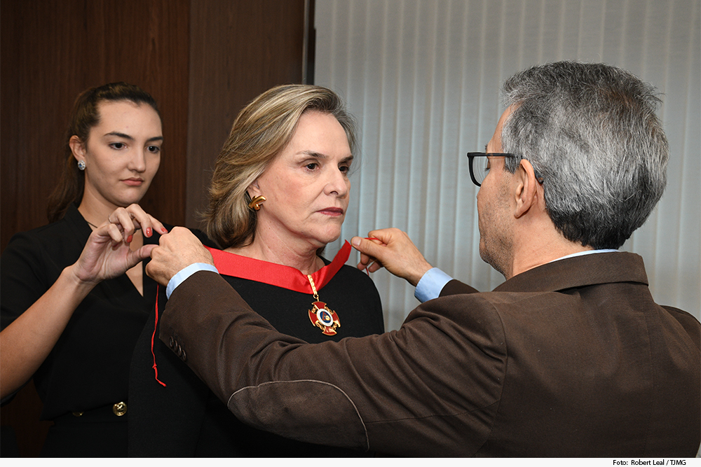 Homem entrega medalha a mulher, ajudado por outra mulher