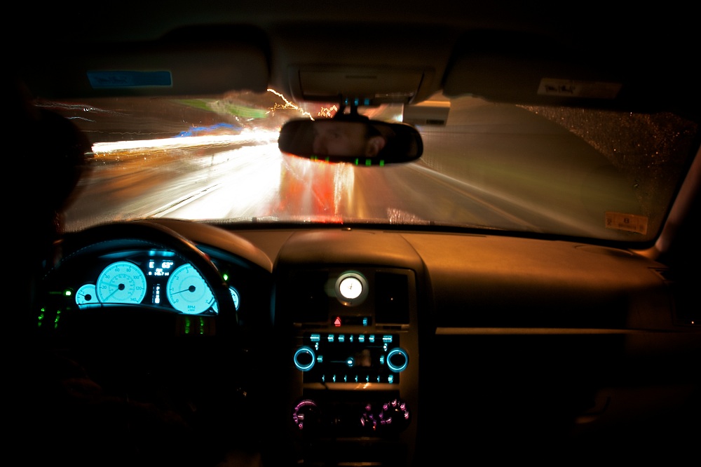 Motorista dentro de carro, em rodovia à noite, com painel iluminado