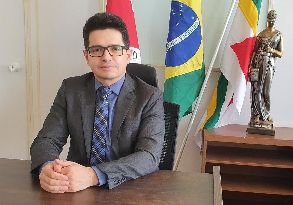 Juiz em ambiente de trabalho, tendo bandeiras e estátua da justiça ao fundo