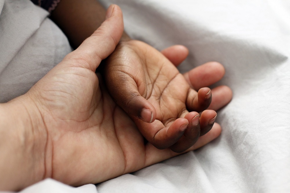 Mão de homem branco pega mãozinha negra de bebê
