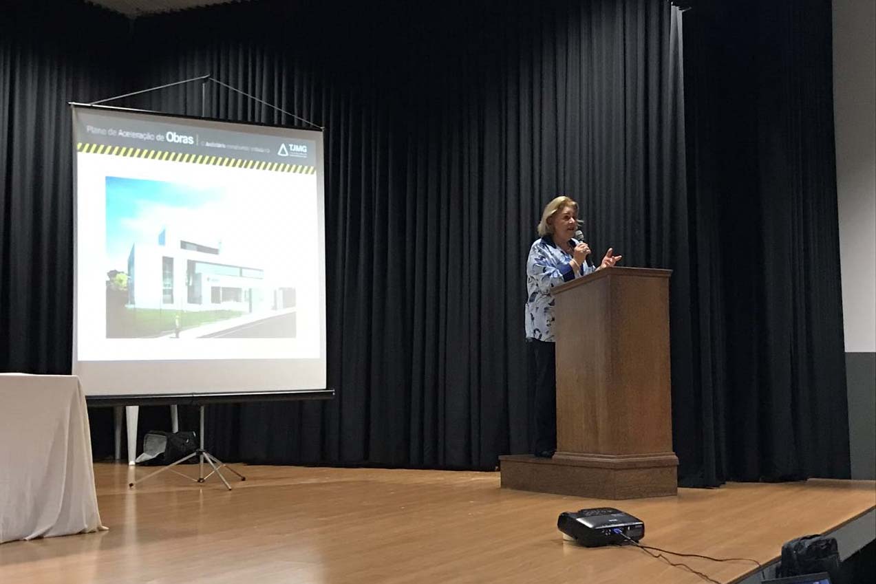 Mulher falando em púlpito e painel atrás dela