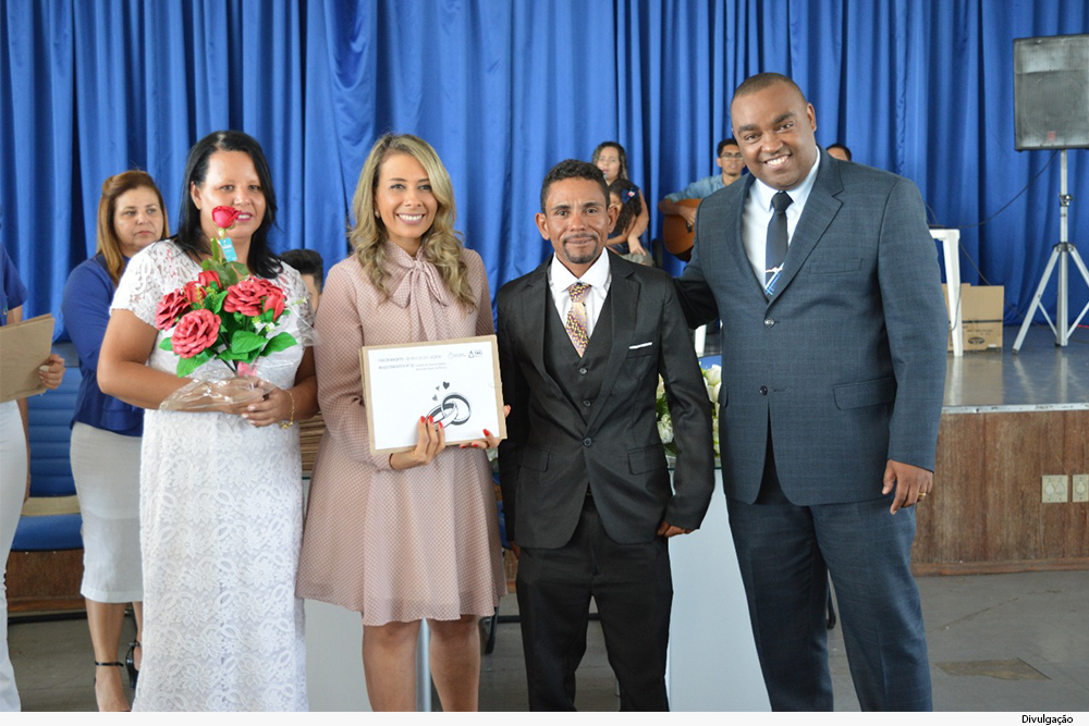 mulher segura buquê de rosas, outra um diploma com gravura de alianças, e mais dois homens de terno