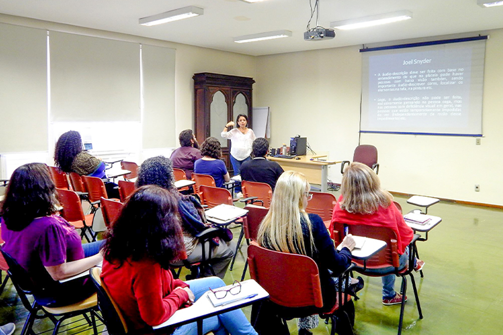 Professora dá aula em sala com estudantes e painel projetado