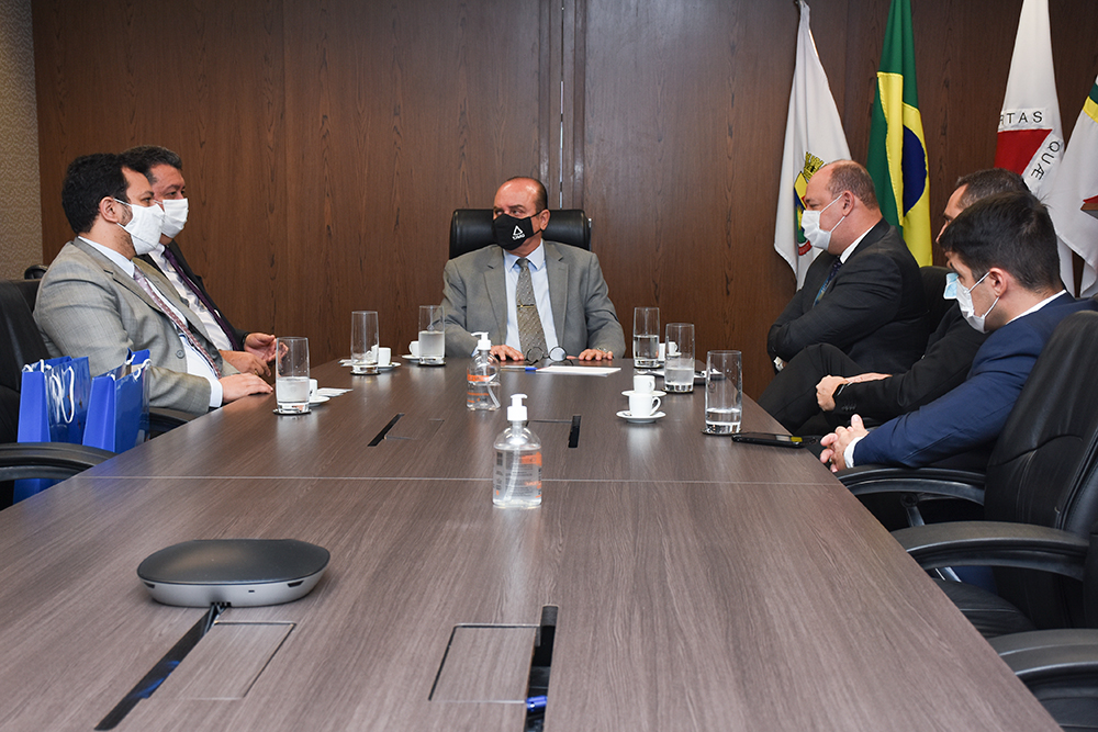 Reunião entre desembargador e visitantes, tendo bandeiras ao fundo